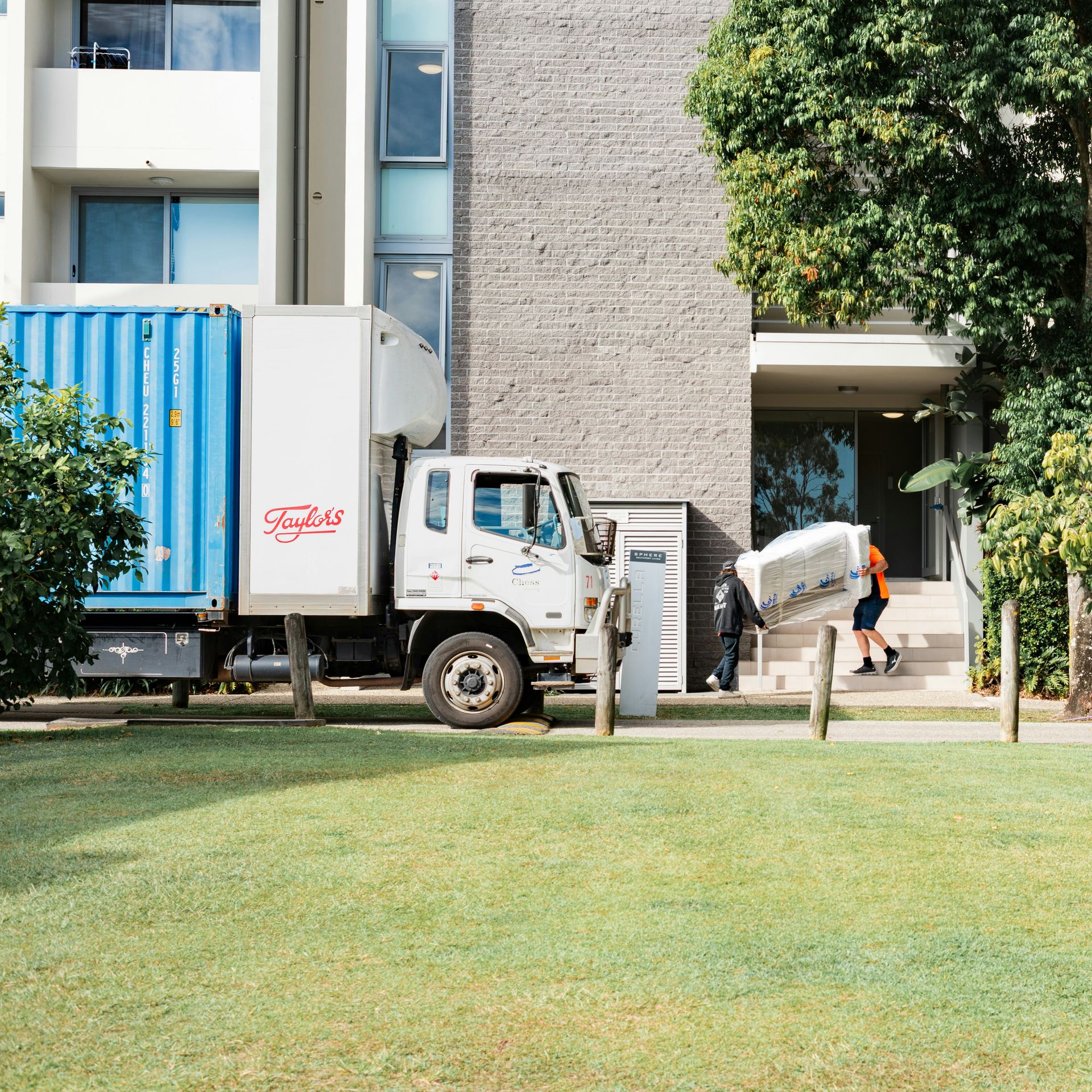 Moving truck and person carrying furniture near a building.